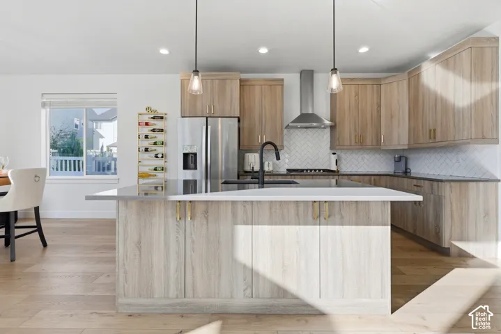 Kitchen featuring wood-finish cabinetry, stainless steel appliances, a white herringbone tile backsplash, an island with countertop seating, and recessed lighting