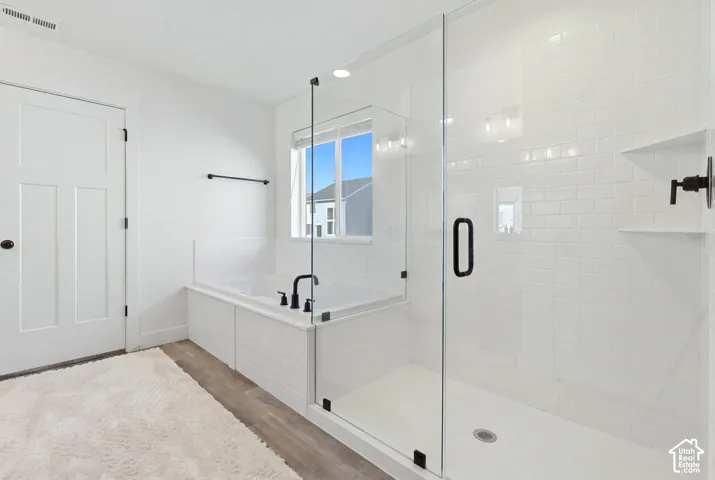 Spa-inspired primary bathroom featuring a frameless glass-enclosed shower with subway tile surround, a soaking tub with deck-mounted faucet, dual vanity with quartz countertop, matte black hardware, and abundant natural light from a large window