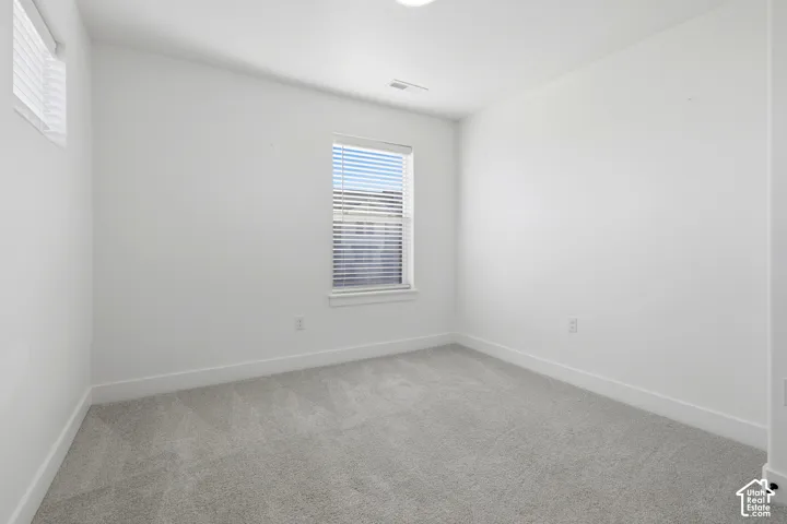 Light gray carpeting, white walls, recessed ceiling light, and two windows with blinds