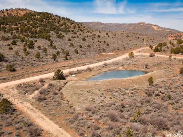 Expansive land parcel featuring a natural pond, rugged dirt roads, and diverse high desert vegetation with distant mountainous terrain
