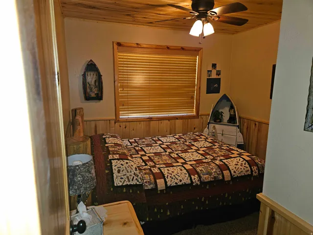 Room featuring wood-paneled walls, wood-finish ceiling, and a ceiling fan with integrated lighting
