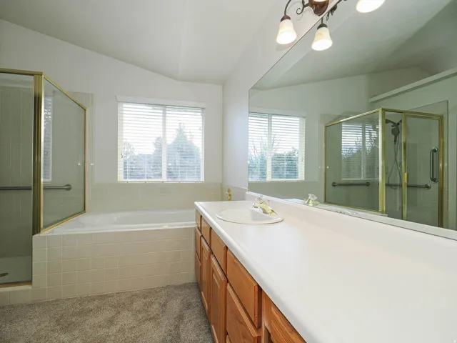Vaulted ceiling with a window, built-in bathtub, glass-enclosed shower, vanity with integrated sink, and large wall-mounted mirror