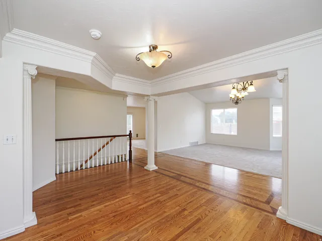 Hardwood flooring with decorative inlay, classic ceiling light fixture, recessed ceiling light fixture, crown molding, and white railing with dark wood handrail