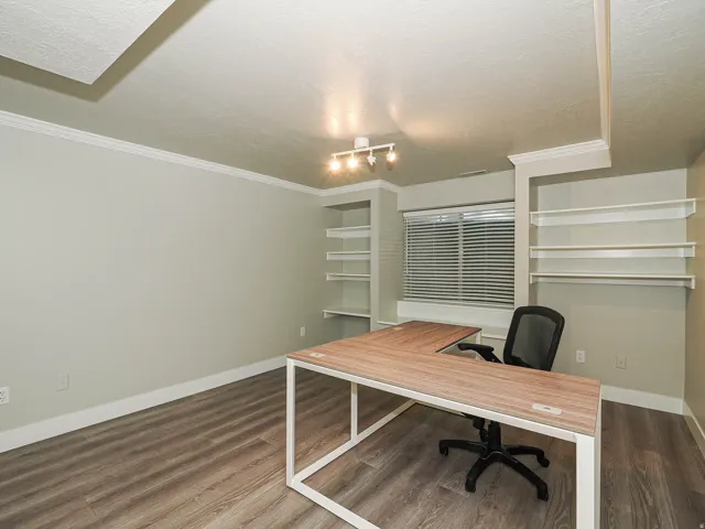 Wood-finish flooring, built-in shelving, crown molding, and a window with blinds