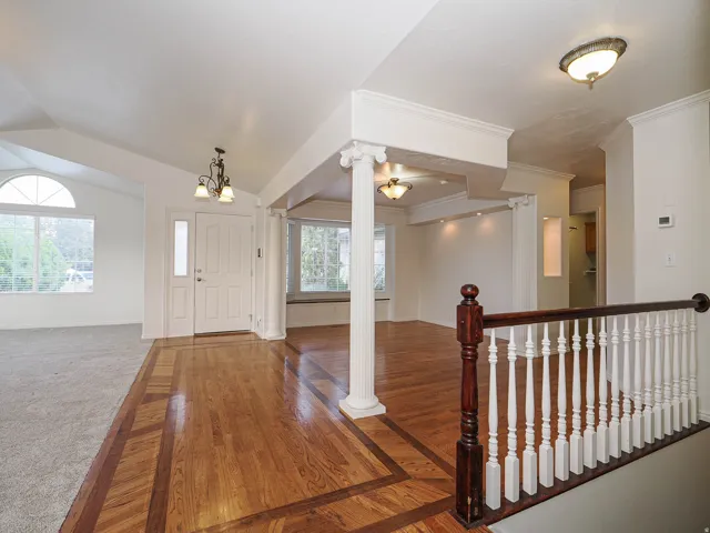 Wood-finish flooring with decorative inlays, white spindle railing with wood newel posts, decorative columns, vaulted ceiling, and an arched window