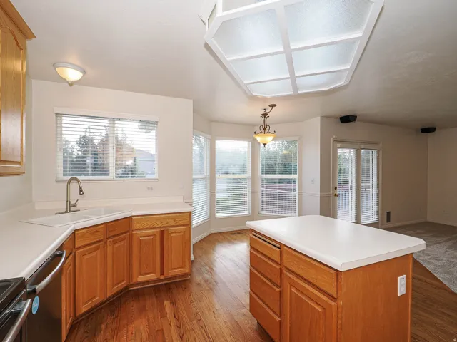 Kitchen featuring wood-finish flooring, wood cabinetry, light countertops, a central island, and a bay window