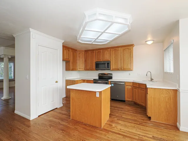 Kitchen featuring wood-finish flooring, wood cabinetry, stainless steel appliances, a center island, and a built-in sink