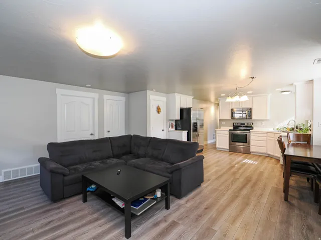 Open-concept living area with wood-finish flooring, white cabinetry, stainless steel appliances, and a dining area