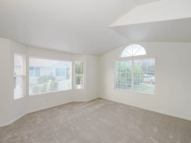 Vaulted ceiling with an arched transom window, bay window with blinds, and neutral carpeting