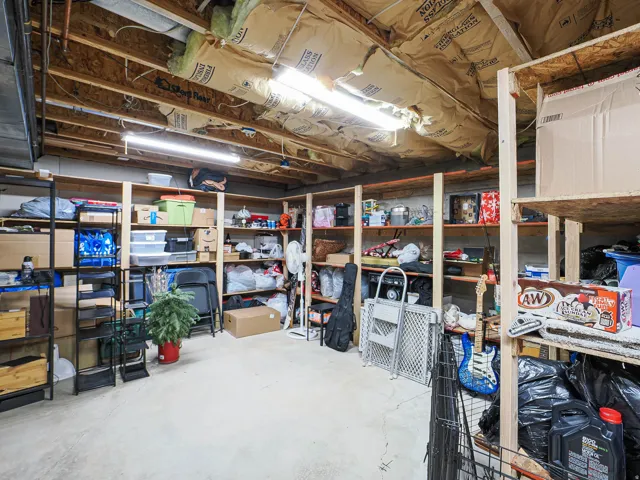 Utility space featuring exposed ceiling joists with insulation, fluorescent lighting, and built-in shelving