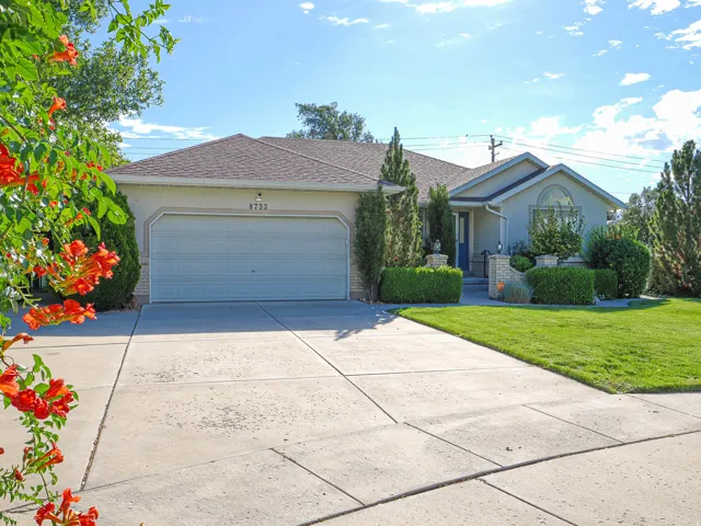 Stucco exterior with an attached garage, arched window, paved driveway, and established landscaping