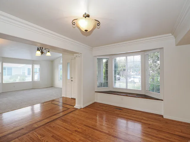 Hardwood flooring with inlaid border, layered crown molding, bay window with integrated window seat, and recessed entry