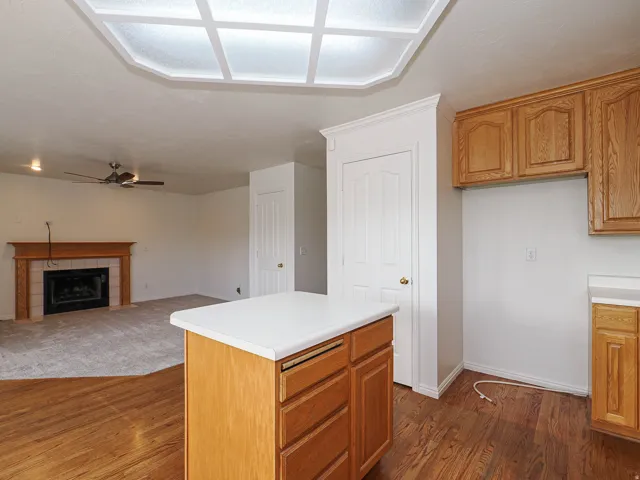 Wood-finish flooring, central kitchen island with countertop, natural wood cabinetry, recessed ceiling light feature, and a fireplace with a wood mantle