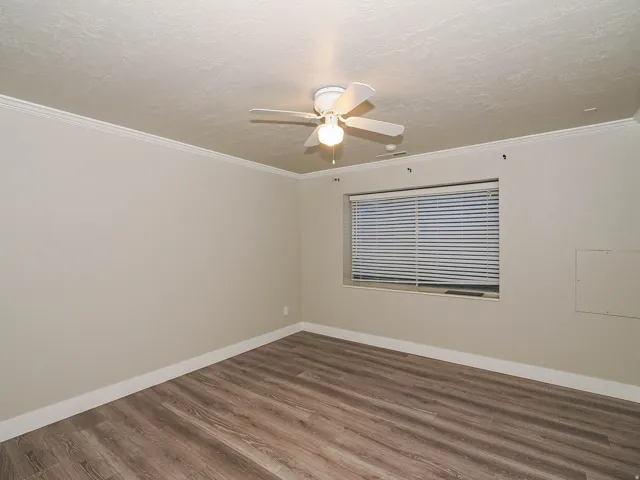 Wood-finish flooring, neutral wall tones, crown molding, and ceiling fan with integrated lighting
