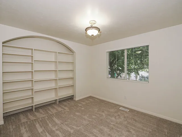 Built-in shelving with an arched top, textured carpeting, window with blinds, and a ceiling-mounted light fixture
