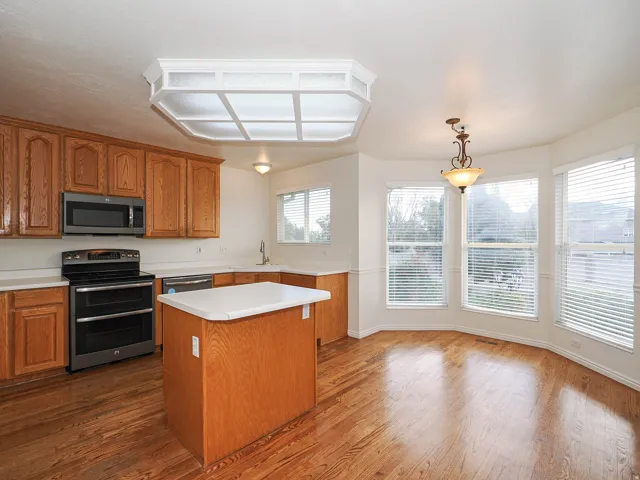 Kitchen featuring wood-finish flooring, wood cabinetry, white countertops, and stainless steel appliances