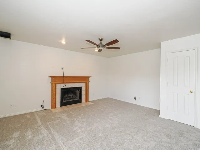 Living area with a wood-mantled fireplace featuring tile surround, recessed lighting, ceiling fan, and carpeted flooring