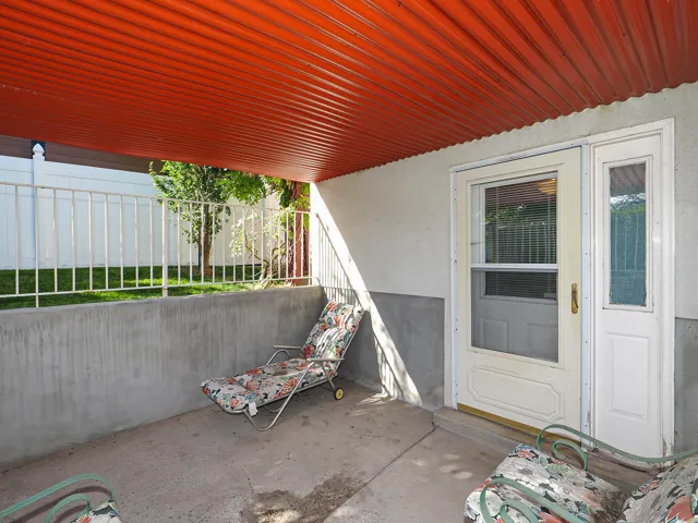 Covered patio featuring a corrugated orange ceiling, concrete flooring, and a white metal fence