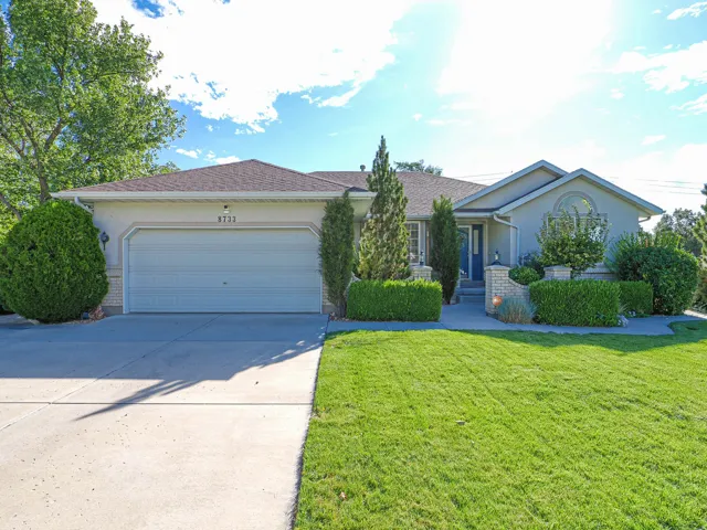 Contemporary stucco exterior with an attached garage, paved driveway, arched window, and mature landscaping