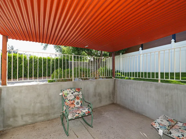 Covered patio area featuring a corrugated metal roof, concrete flooring, concrete walls, and a white metal fence