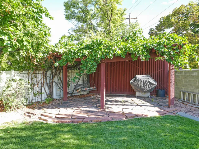 Stone paver patio with a wood pergola, lush overhead foliage, and a manicured lawn