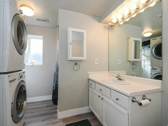 Bathroom featuring a stacked laundry unit, a single vanity with an integrated sink, a large wall-mounted mirror, and wood-finish flooring