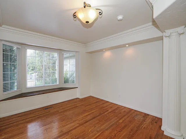 Hardwood-finish flooring, bay window with integrated window seat, decorative ceiling light fixture, recessed wall lighting, and fluted column detailing