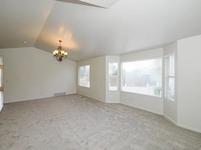Vaulted ceiling with an ornamental chandelier, bay window with blinds, secondary windows, and carpeted flooring