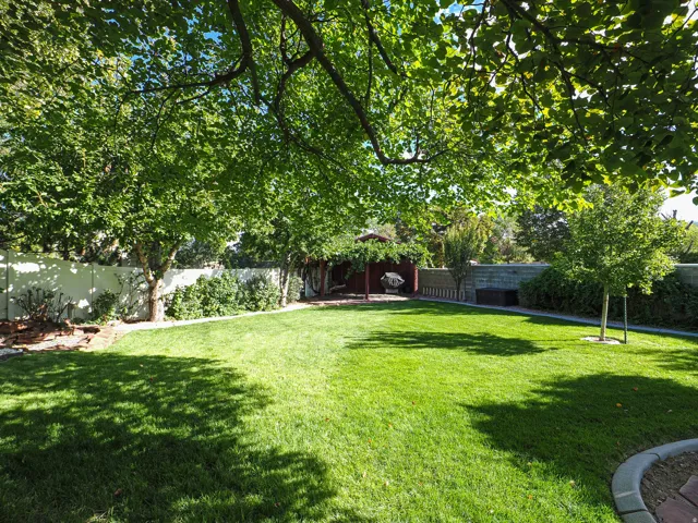 Expansive lawn area with mature trees, a privacy fence, and concrete block wall