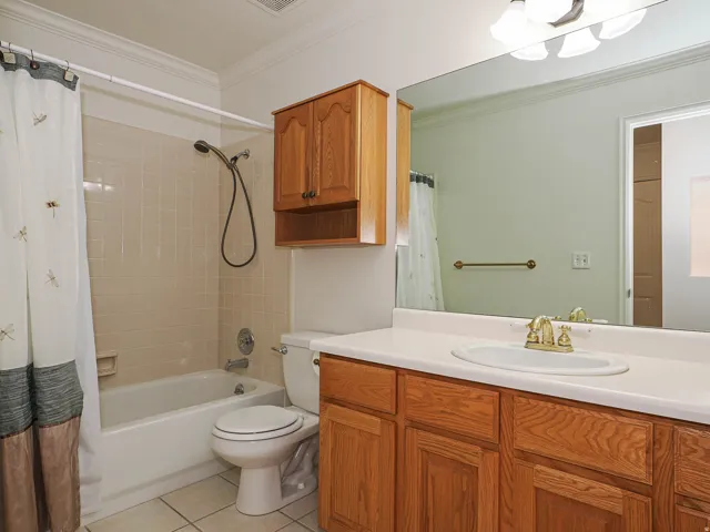 Bathroom featuring a built-in bathtub with tiled surround, a toilet, a vanity with a white countertop and integrated sink, a wall-mounted mirror, and wood-finish cabinetry