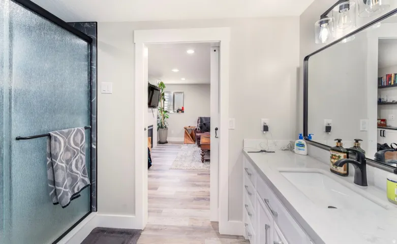 Bathroom featuring a single vanity with an undermount sink, a large framed mirror, a three-light vanity fixture, and a glass-enclosed shower with black trim