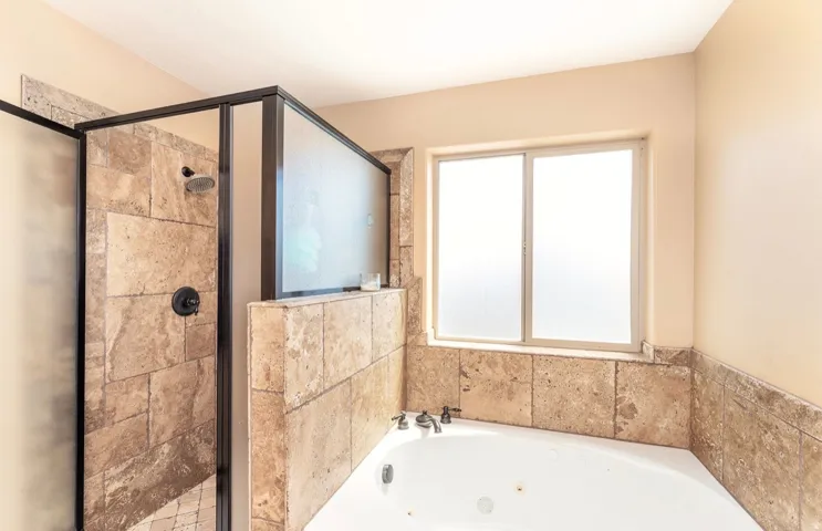 Corner jetted soaking tub and walk-in shower with stone tile surround