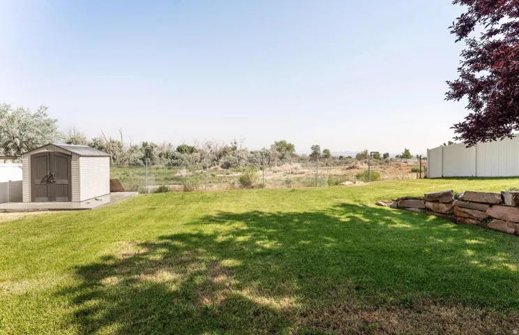 Expansive lawn with a storage shed on a concrete pad, a white vinyl privacy fence, and a stone retaining wall