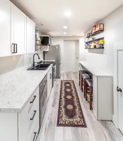 Galley kitchen featuring white cabinetry, light-toned wood-finish flooring, and a stone-finish countertop