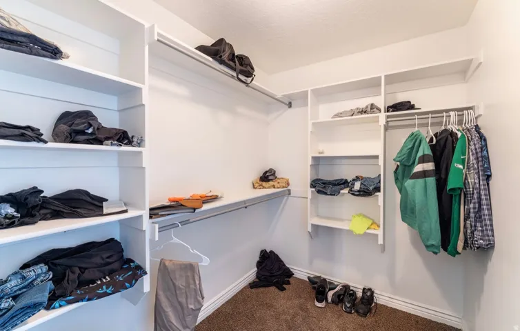 Spacious walk-in closet featuring white built-in shelving, multiple hanging rods, and neutral-toned carpeting
