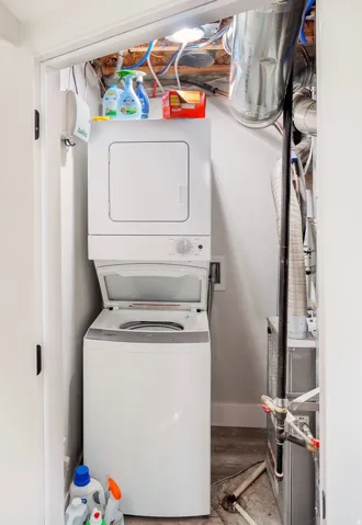 Dedicated utility closet featuring a stacked white washer and dryer unit, wood-finish flooring, and exposed mechanicals