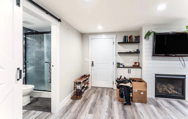 Spacious room featuring wood-finish flooring, a built-in fireplace, and a barn door leading to a bathroom with a glass-enclosed shower
