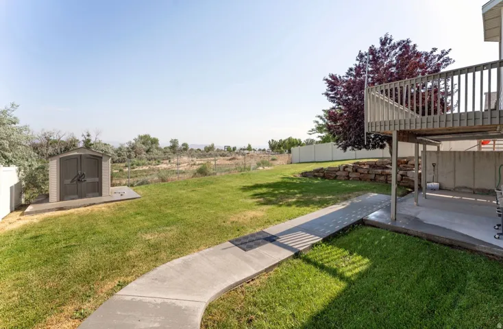 Expansive backyard featuring a manicured lawn, a detached storage shed on a concrete pad, and a curved concrete pathway