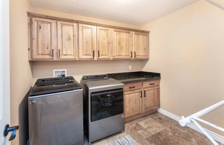 Laundry area featuring wood-finish cabinetry, black stone-look countertops, and neutral-toned wall paint