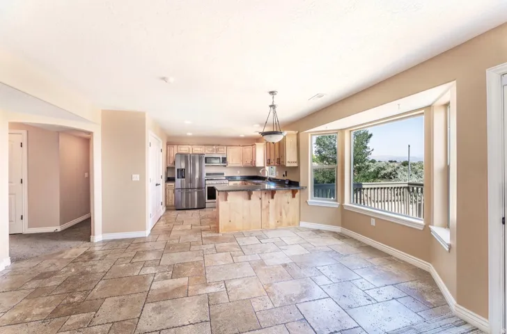 Open-concept kitchen and dining area featuring large format tile flooring, light wood cabinetry, stainless steel appliances, and a bay window overlooking an outdoor deck