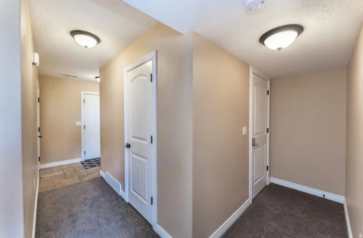 Hallway featuring neutral wall paint, white trim, recessed panel doors, overhead lighting, and contrasting carpet and tile flooring