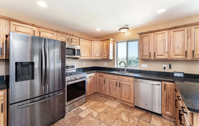 Kitchen featuring natural wood cabinetry, dark countertops, and stainless steel appliances