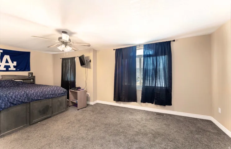 Spacious bedroom featuring neutral wall tones, textured carpeting, and a ceiling fan with integrated lighting