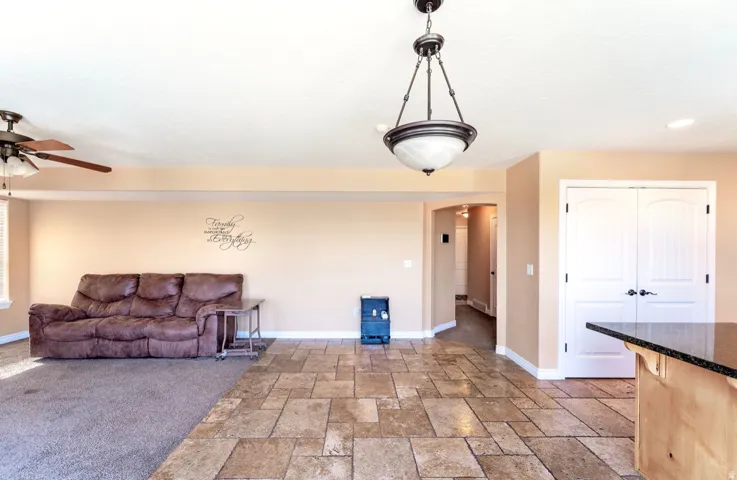 Expansive room featuring a combination of square tile flooring and carpet, neutral wall tones, a ceiling fan, and a chandelier