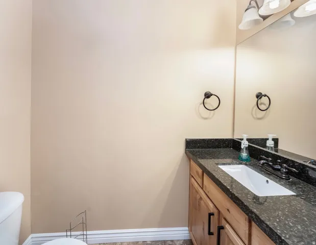 Bathroom vanity featuring a dark speckled countertop, an integrated rectangular sink, and wood-finish cabinetry with dark hardware