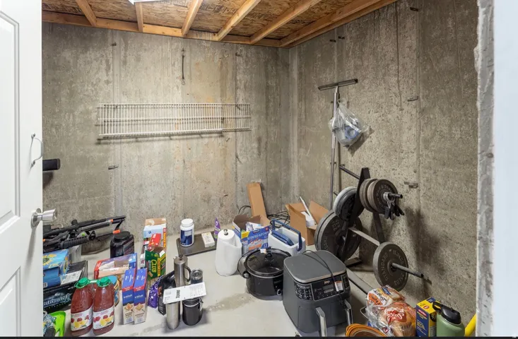Unfinished basement space featuring exposed concrete walls and an open ceiling with visible wood joists