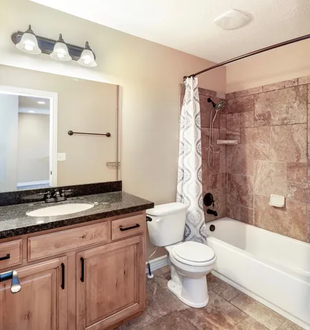 Bathroom featuring a vanity with wood-finish cabinetry and a dark stone countertop, an undermount sink with a dark-finish faucet, and a large mirror