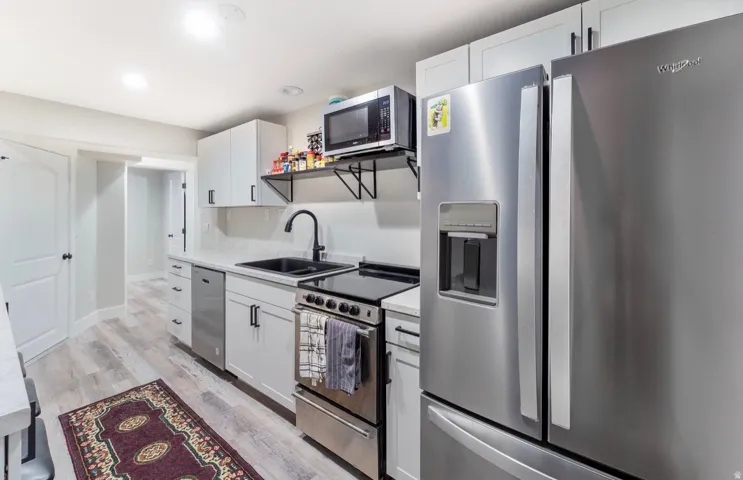 Modern kitchen featuring stainless steel appliances, white cabinetry with black hardware, light-toned wood-finish flooring, and recessed lighting
