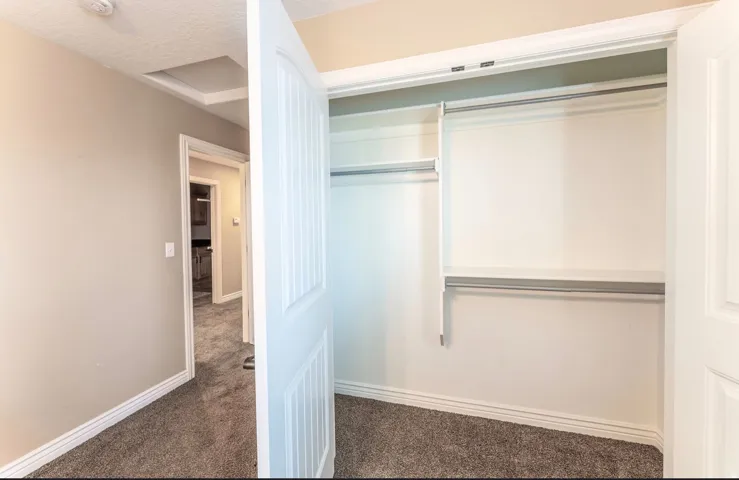 Neutral-toned room featuring a closet with bi-fold doors, upper shelving, and two clothing rods