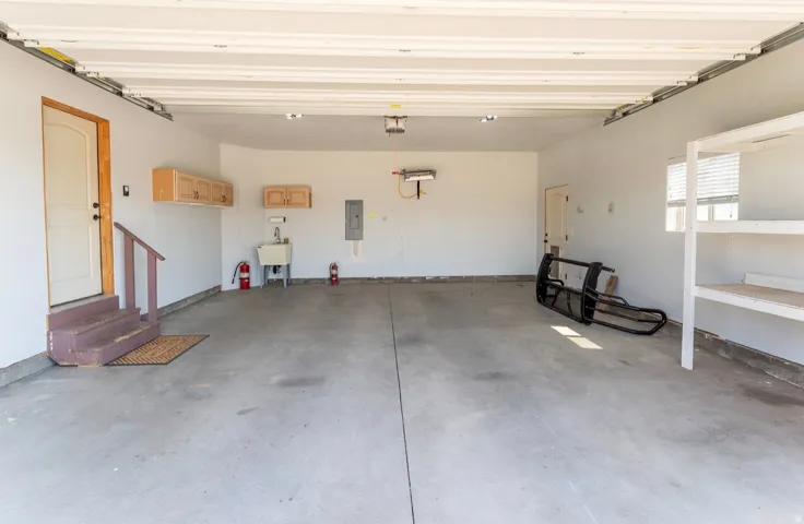 Spacious garage featuring a concrete floor, utility sink, built-in cabinetry, and integrated shelving